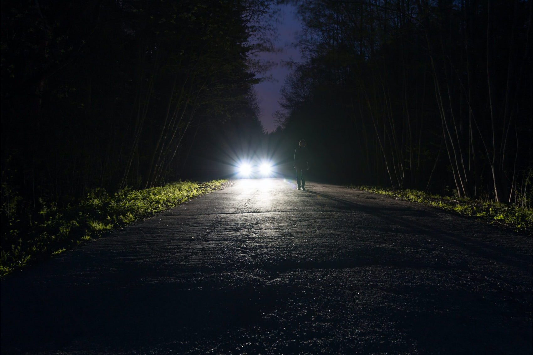 Front view of headlight beams in the distant at night on a dark road.